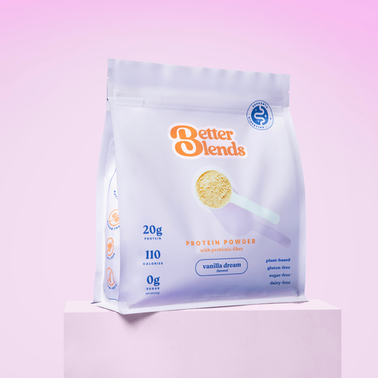 A hand pours Gutty Chocolate Swirl protein powder into a glass of shake with a striped straw, next to a bright yellow-green better blends protein bag on an orange background.